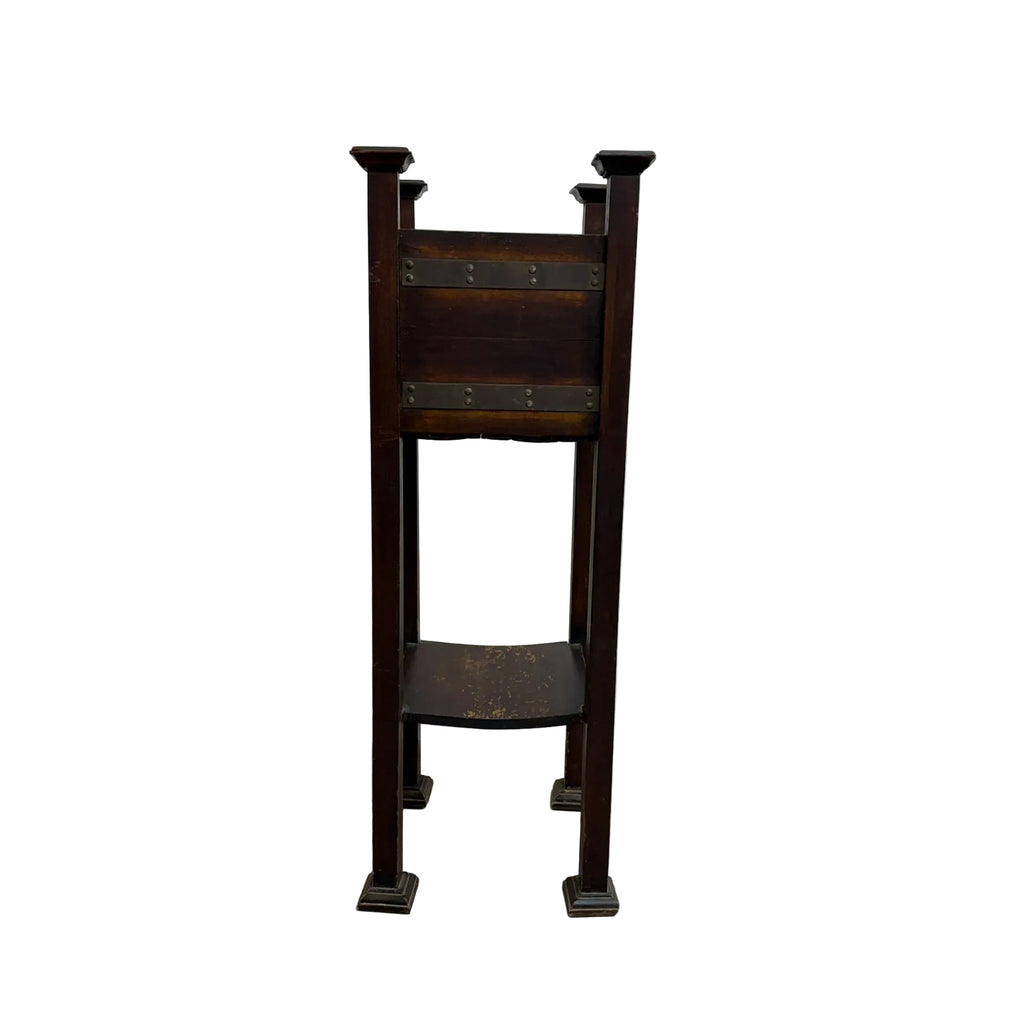 A vintage dark brown wooden stand or easel with metal brackets and legs, photographed against a plain white wall and concrete floor.