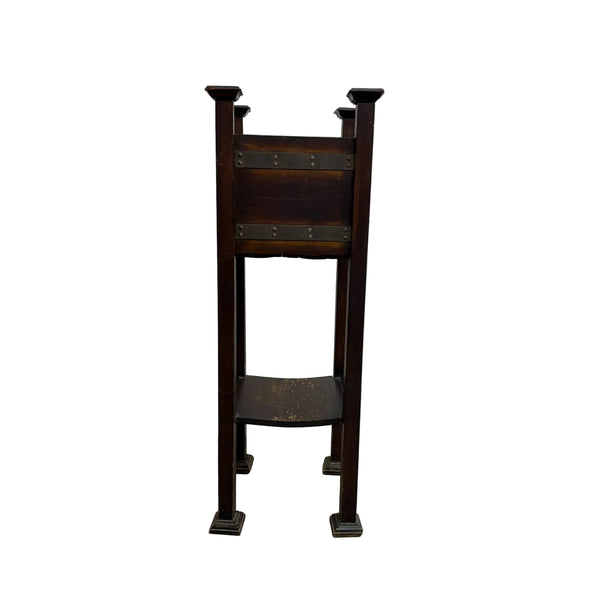 A vintage dark brown wooden stand or easel with metal brackets and legs, photographed against a plain white wall and concrete floor.