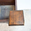 A close-up of a square wooden drawer pull handle with a distressed brown finish and dark edges, attached to a dark wooden furniture piece.