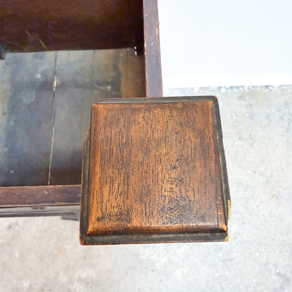 A close-up of a square wooden drawer pull handle with a distressed brown finish and dark edges, attached to a dark wooden furniture piece.