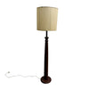 A vintage-style floor lamp with a dark brown wooden pedestal base and a vinyl   shade, standing on a concrete floor against a white wall.