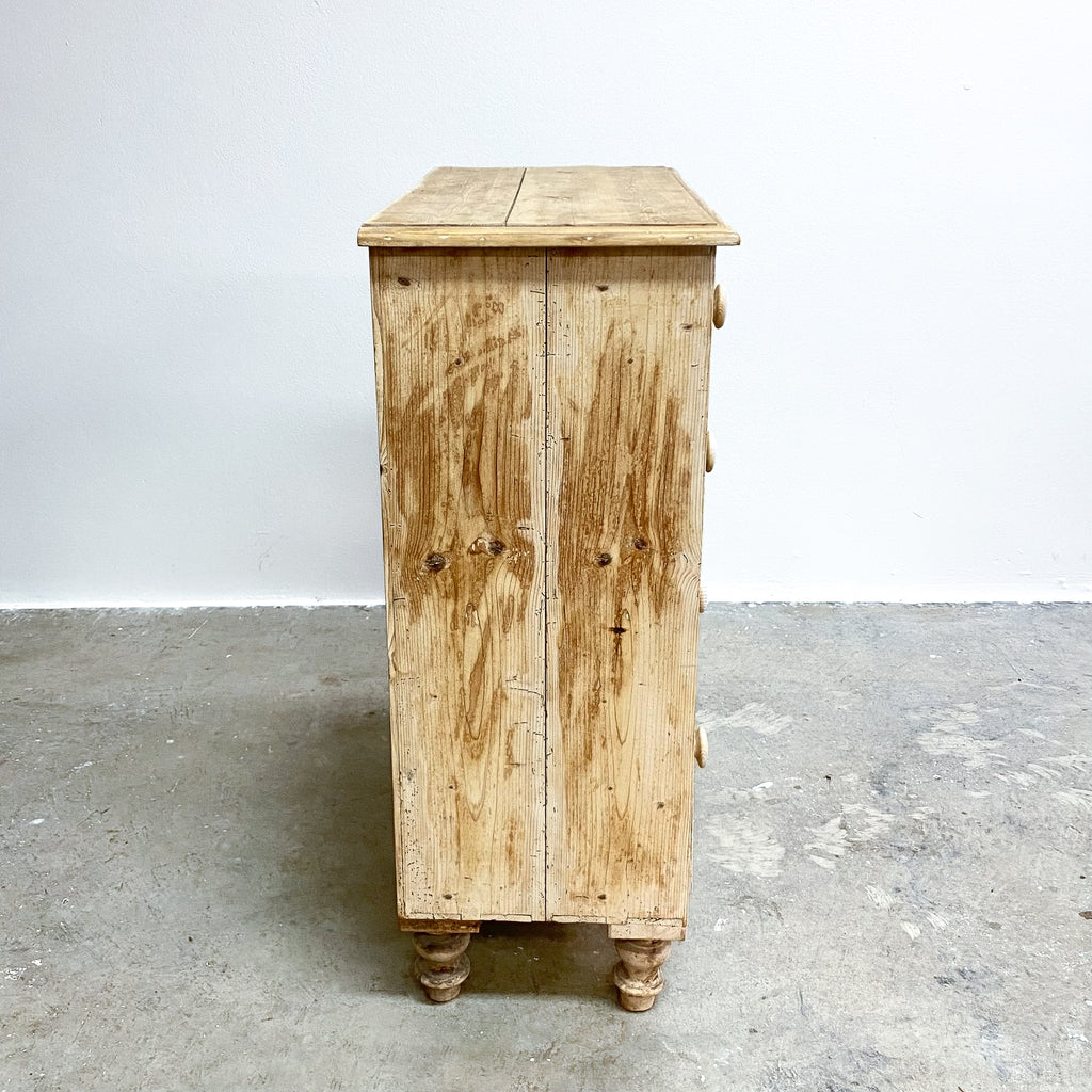 Wooden cabinet with a rustic finish on a concrete floor against a white wall