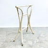 White metal stool with a minimalist design on a gray concrete floor.