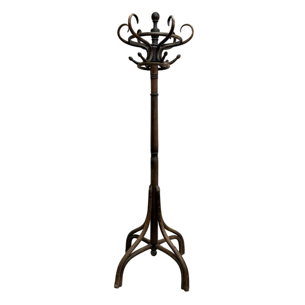 A dark brown wooden coat rack with a multi-hook top and a tripod-style base, standing on a concrete floor against a plain white wall.