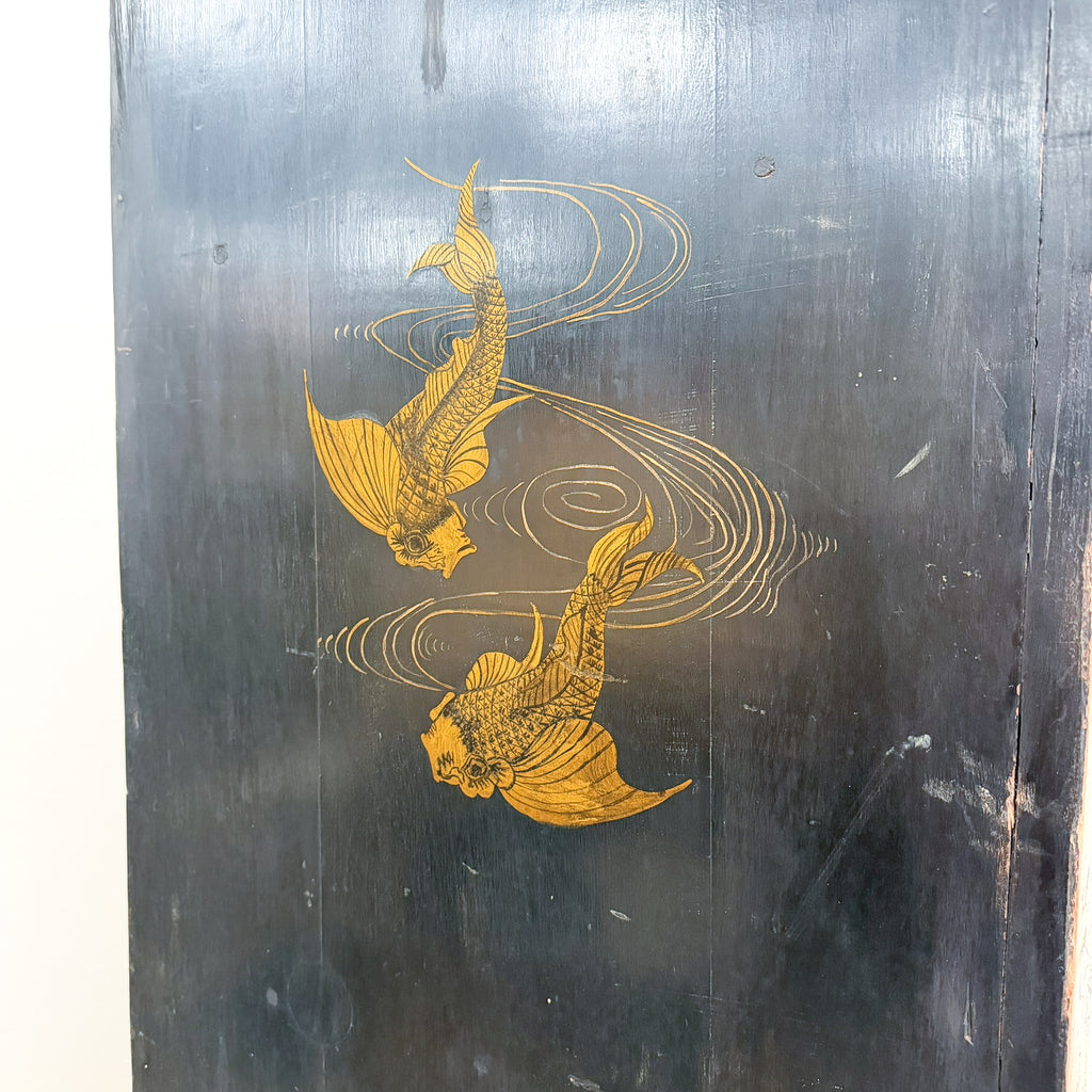A dark, weathered black wooden panel featuring a hand-painted golden koi fish design with swirling water lines.