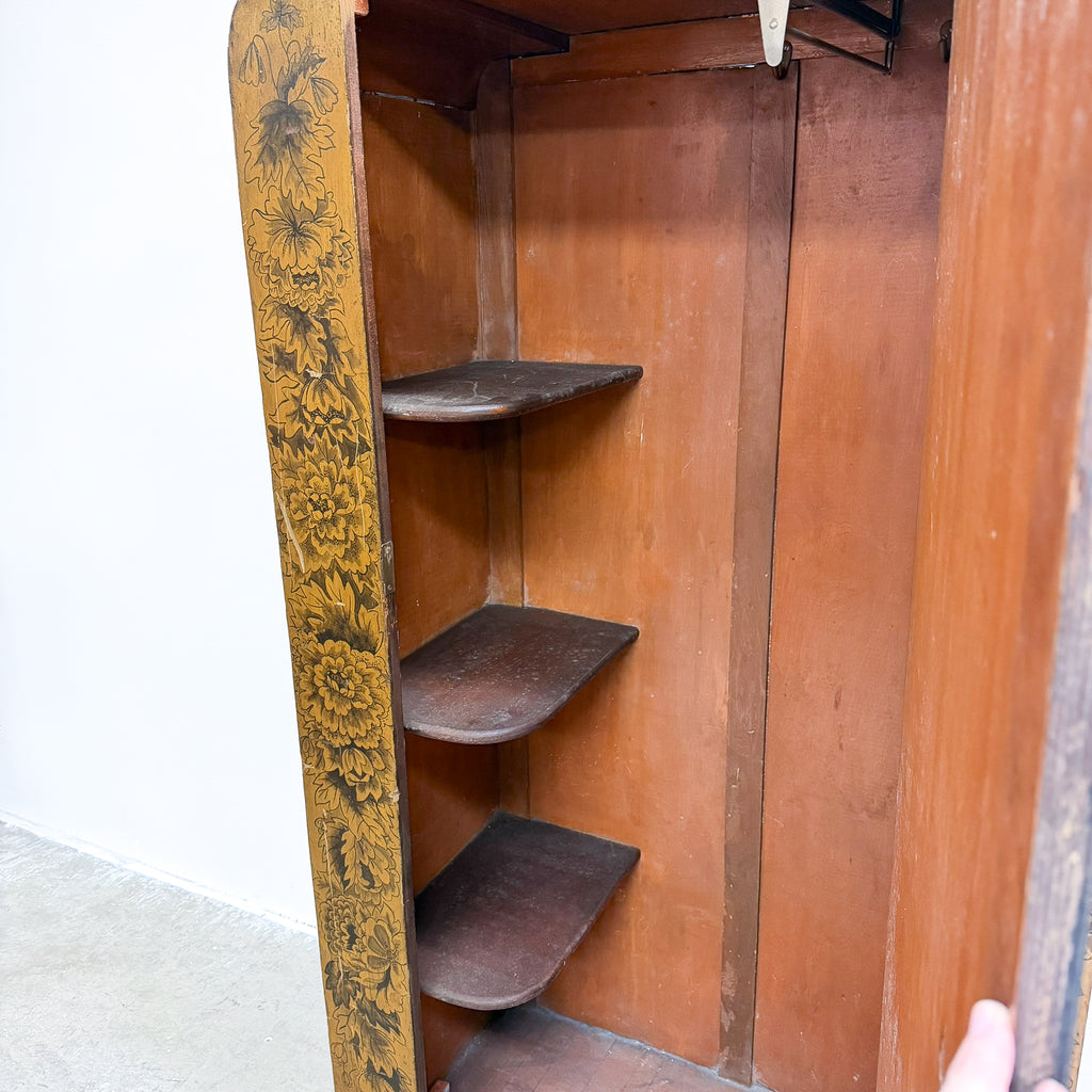 An antique wooden corner cabinet or closet organizer with three built-in shelves, featuring a gold and black floral painted side panel and a warm brown wood interior.