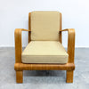 A mid-century modern lounge chair with curved wooden arms and legs, upholstered in a light beige textured fabric, set against a plain white wall and gray concrete floor.