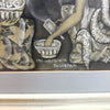 A close-up of a framed artwork showing a stylized figure in patterned clothing reaching into a bowl, with the text 'ini warpiana Peliatan' written near the bottom. The frame and mat are visible, and the artwork uses muted beige, gray, black, and white tones.