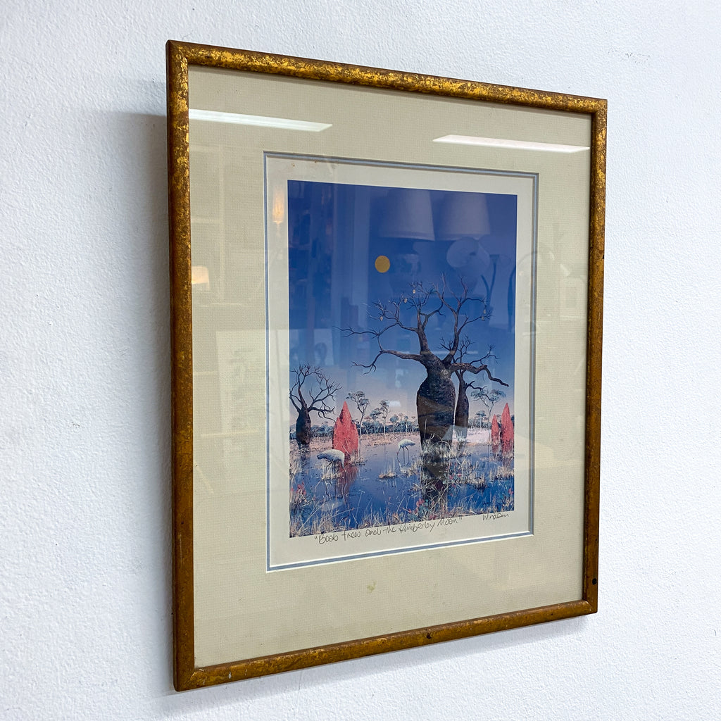 Framed artwork of a tree with a blue sky background on a white wall.