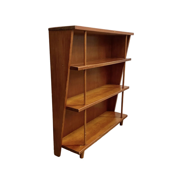 Wooden bookshelf with three shelves on a gray floor against a white wall