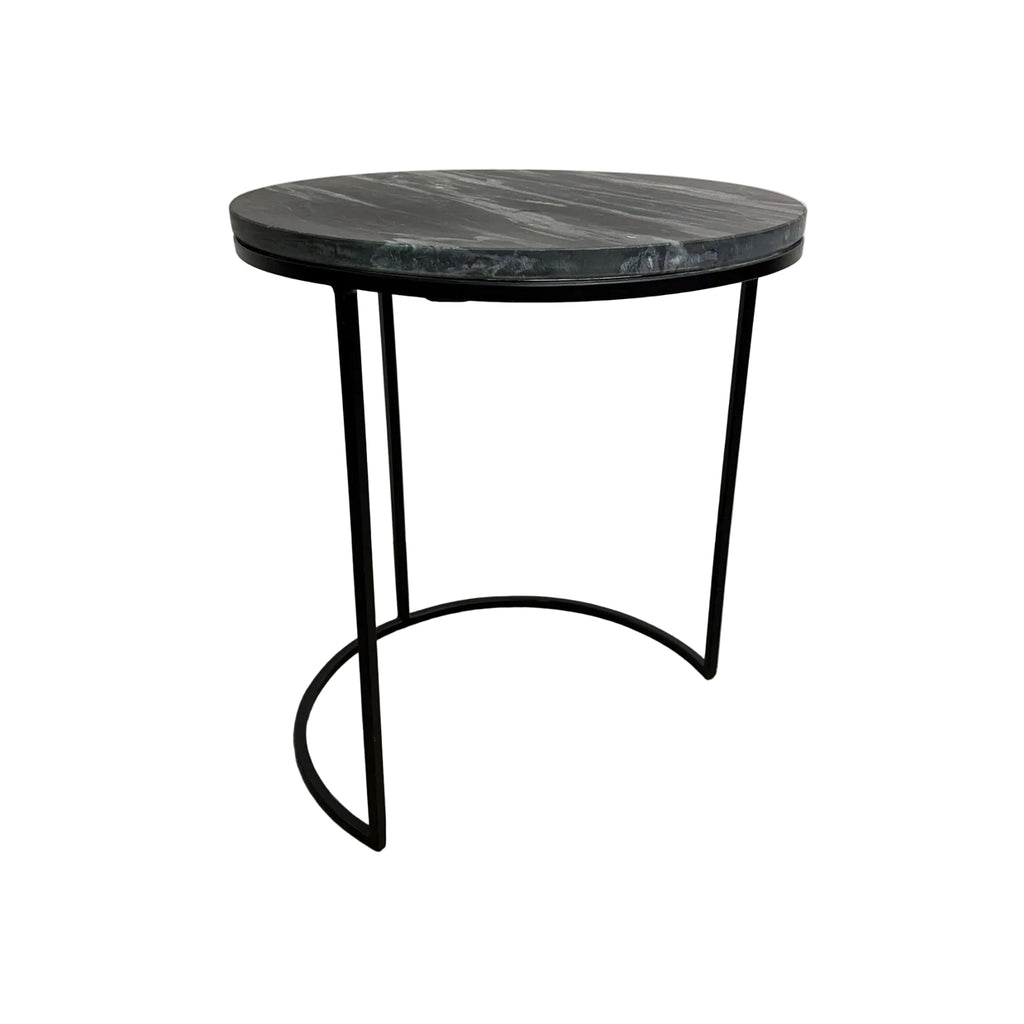A round side table with a dark gray marble top and a black metal frame with a curved base, set against a plain white wall and concrete floor.