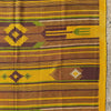 A close-up of a woven textile with horizontal stripes and geometric motifs in yellow, brown, olive green, and cream, photographed against a stone surface.