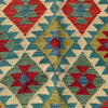 A close-up of a woven textile with a geometric kilim pattern in red, teal, sage green, mustard yellow, and cream.