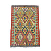 A rectangular kilim rug with a colorful geometric diamond pattern, laid flat on a textured gray concrete surface.