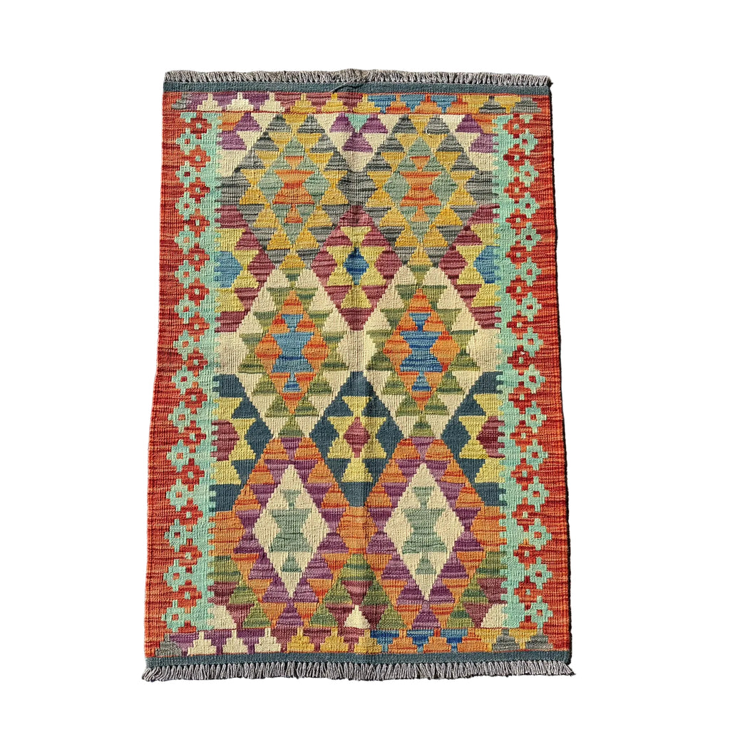 A rectangular kilim rug with a colorful geometric diamond pattern, laid flat on a textured gray concrete surface.