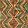 A close-up of a woven textile with a geometric diamond pattern in orange, olive green, gray, beige, and mustard yellow.
