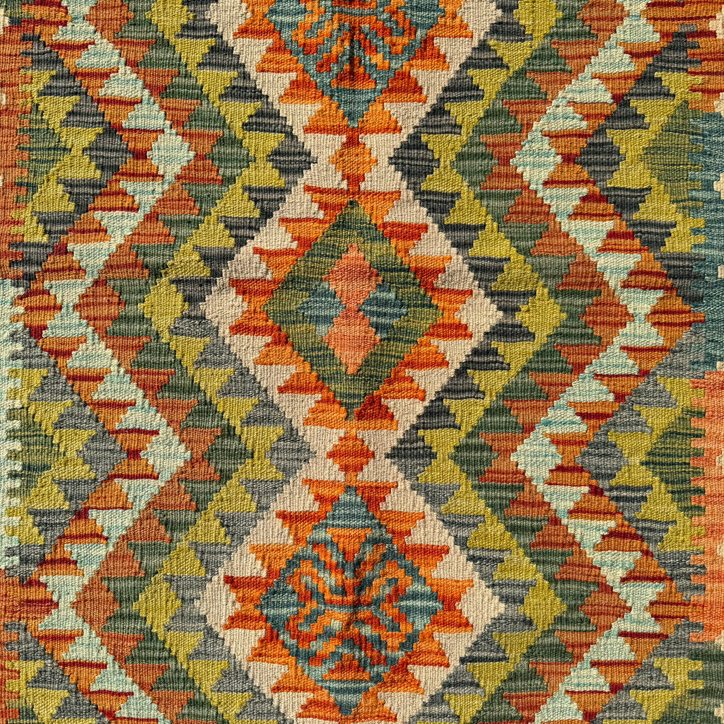 A close-up of a woven textile with a geometric diamond pattern in orange, olive green, gray, beige, and mustard yellow.