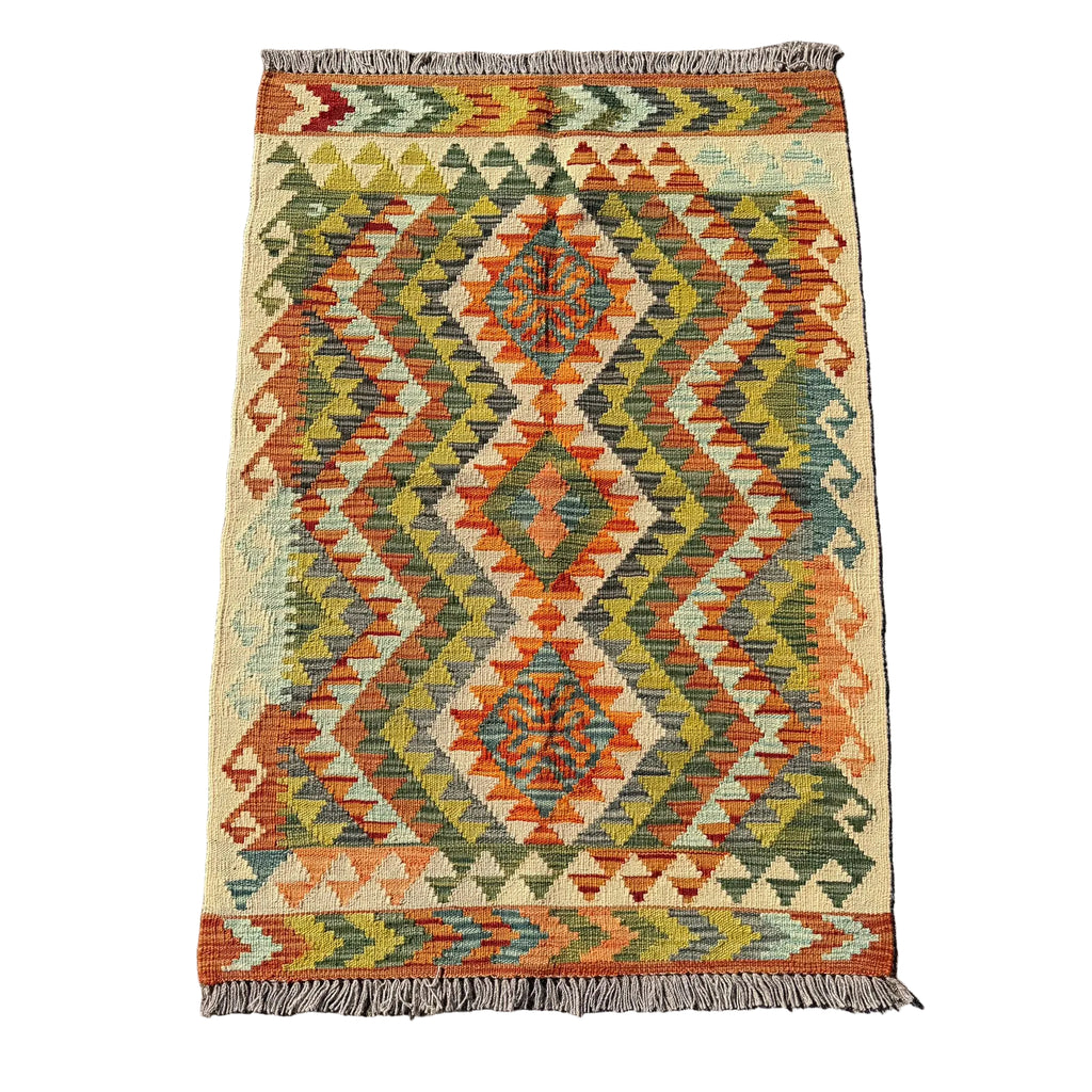 A rectangular woven kilim rug with a geometric diamond pattern in orange, olive green, beige, and blue, laid flat on a gray concrete surface.