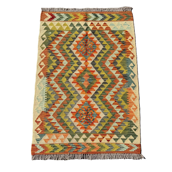 A rectangular woven kilim rug with a geometric diamond pattern in orange, olive green, beige, and blue, laid flat on a gray concrete surface.