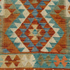 A close-up of a woven textile with a geometric diamond pattern in rust orange, teal blue, cream, and muted olive green.