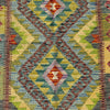 A close-up of a woven geometric rug with a Southwestern-style diamond pattern in muted green, blue, yellow, brown, and red tones.