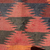 A close-up of a woven textile with a geometric pattern in terracotta red, dark charcoal gray, and orange, showing the detailed texture of the fabric.