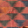 A close-up of a woven textile with a geometric pattern in terracotta pink, orange, dark green, and navy blue.