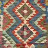 A close-up of a woven kilim textile with a geometric diamond pattern in red, blue, gray, green, pink, and cream.