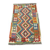 A rectangular kilim rug with a multicolor geometric diamond pattern, laid flat on a gray concrete surface.