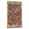 A square woven area rug with a vibrant geometric diamond pattern in multiple colors including orange, teal, red, purple, and green on a cream background, finished with fringed edges.