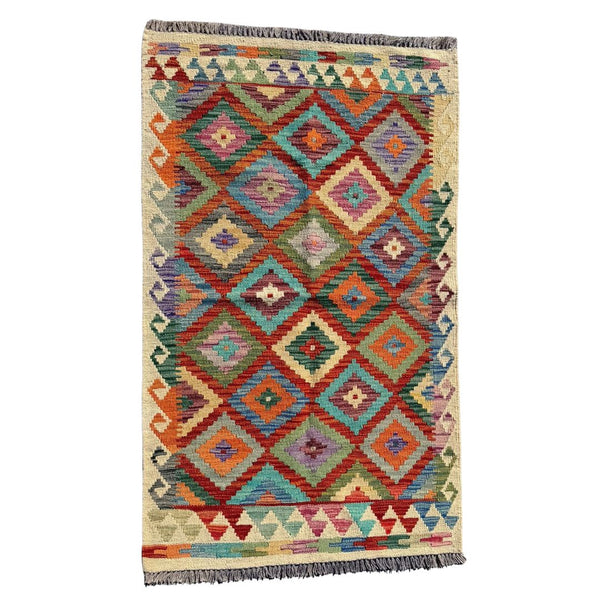 A square woven area rug with a vibrant geometric diamond pattern in multiple colors including orange, teal, red, purple, and green on a cream background, finished with fringed edges.