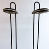 A pair of vintage black metal floor lamps with hexagonal shades and U-shaped top bars, set against a plain white wall.