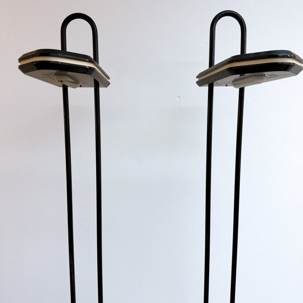 A pair of vintage black metal floor lamps with hexagonal shades and U-shaped top bars, set against a plain white wall.