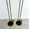 A pair of vintage black metal floor lamps with thin uprights and round bases, standing on a concrete floor against a white wall.