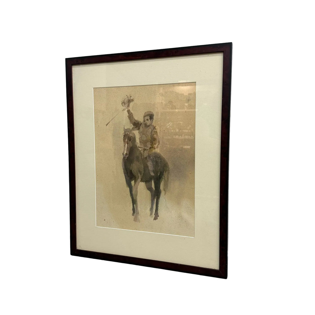 A framed vintage art print depicting a jockey riding a horse and waving, set in a dark brown frame with a cream mat, leaning against a white wall on a concrete floor.