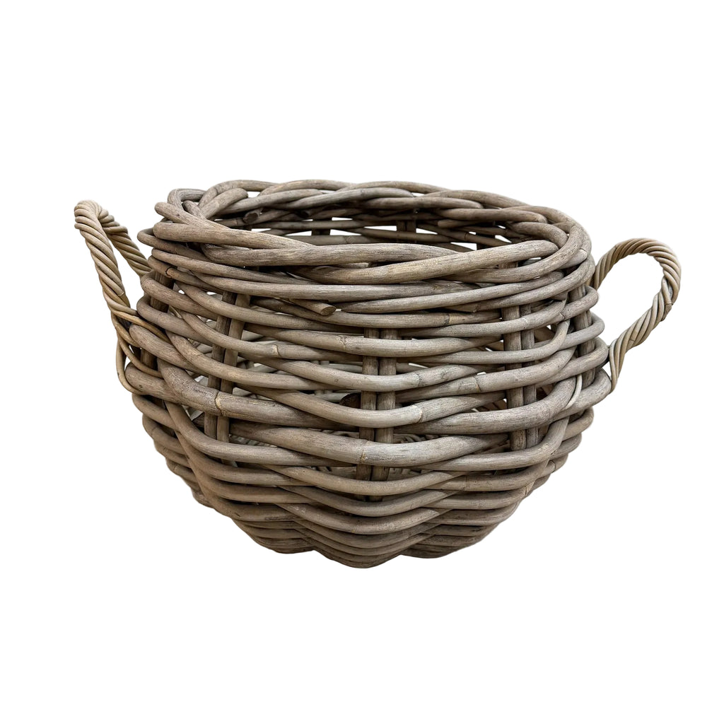 A round woven wicker basket with two twisted side handles, shown on a light gray concrete floor against a white wall.