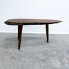 A mid-century modern live-edge wooden coffee table with a dark brown top and legs, set against a plain white wall and concrete floor.