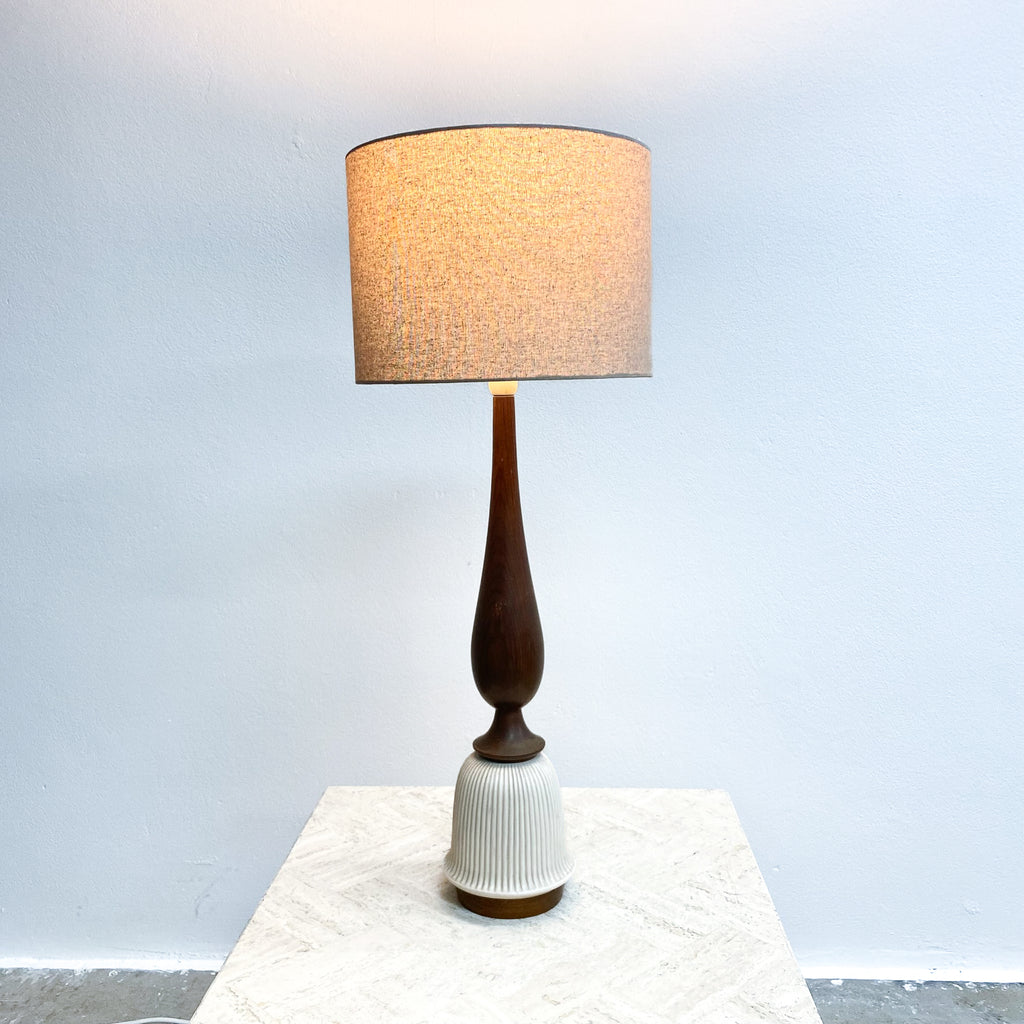 Table lamp with a wooden base and beige shade on a white surface against a light blue background