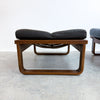 A mid-century modern lounge chair with a curved wooden frame and a black leather cushion, photographed in a minimalist room with a concrete floor and white wall.