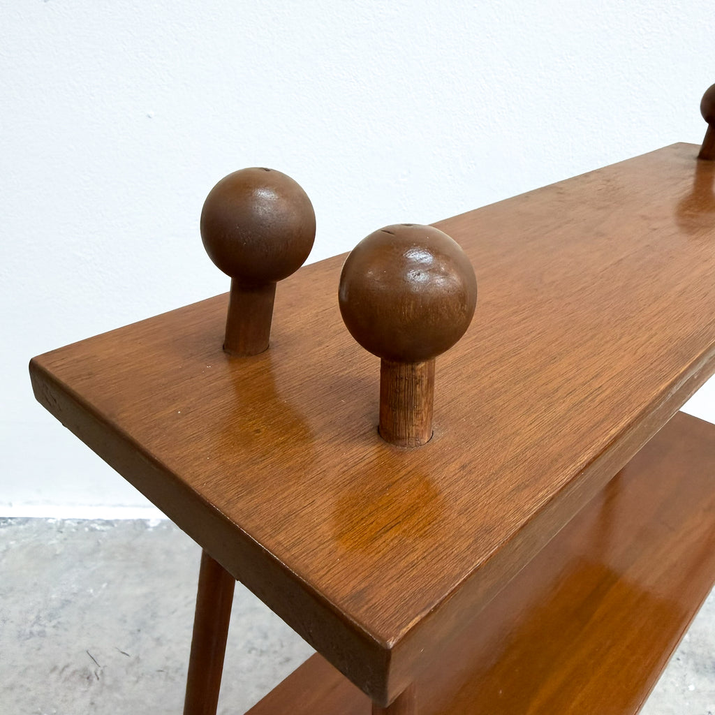 A close-up of a mid-century modern wooden console table with a warm brown finish, featuring two spherical wooden pegs on the top surface and a lower shelf.