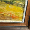 Close-up of a framed painting showing textured impasto brushstrokes in yellow, green, orange, and brown, with a visible artist signature near the bottom.