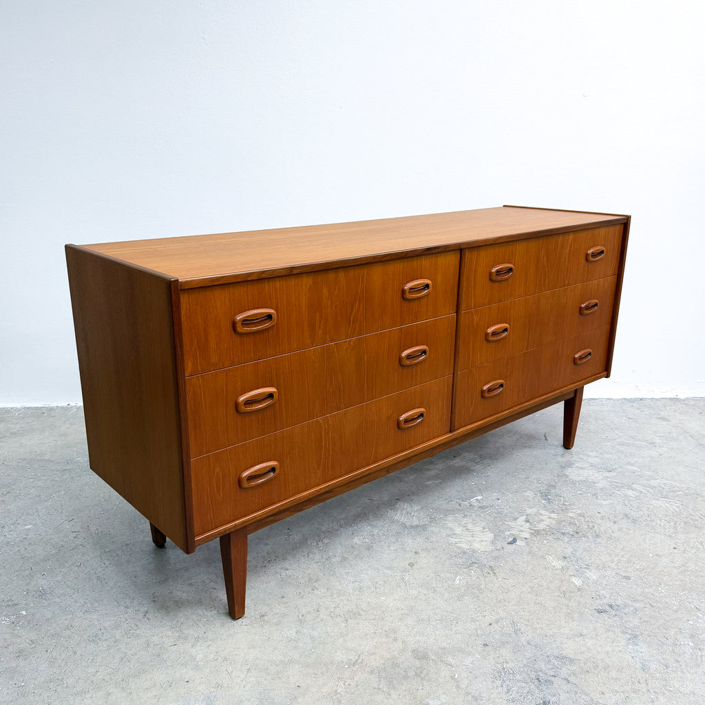 Mid-century modern wooden sideboard with six drawers, shown on a concrete floor against a plain light gray wall.