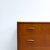 A close-up of a mid-century modern wooden dresser with two drawers and oval wood pulls, set against a plain white wall.