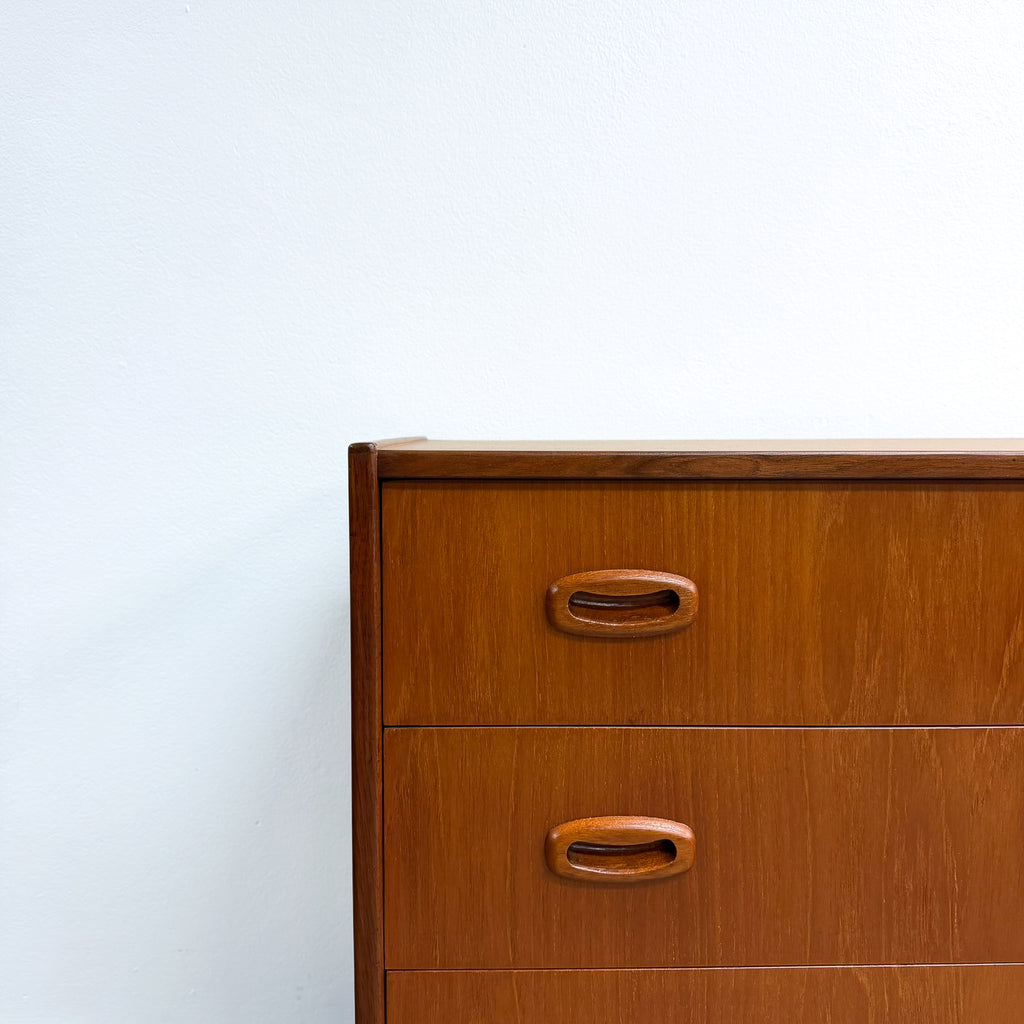A close-up of a mid-century modern wooden dresser with two drawers and oval wood pulls, set against a plain white wall.