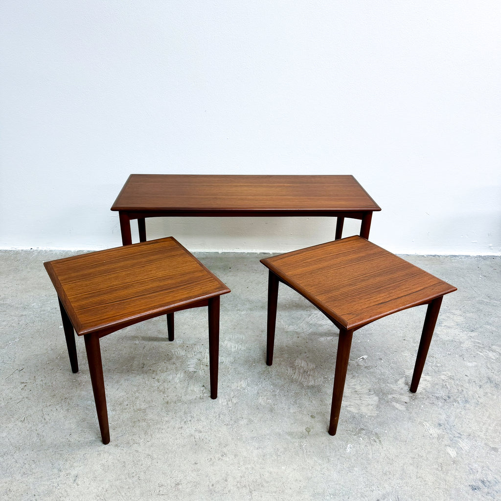 Set of three wooden nesting tables on a concrete floor with a white wall background