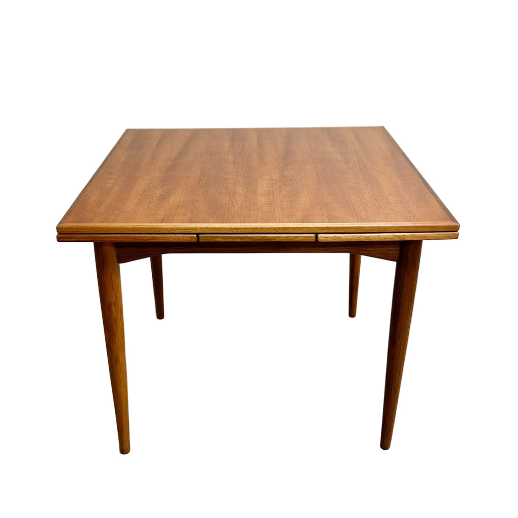 Wooden dining table with a single extension leaf on a gray floor.