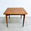 Wooden dining table with a single extension leaf on a gray floor.