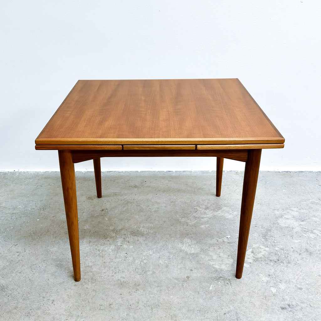 Wooden dining table with a single extension leaf on a gray floor.
