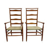 Two matching mid-century modern wooden dining chairs with ladder-back designs, armrests, and woven seat cushions, set against a plain white wall and concrete floor.