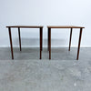 Two matching mid-century modern wooden tables with dark brown walnut-look tops and tapered legs, set against a plain white wall and concrete floor.
